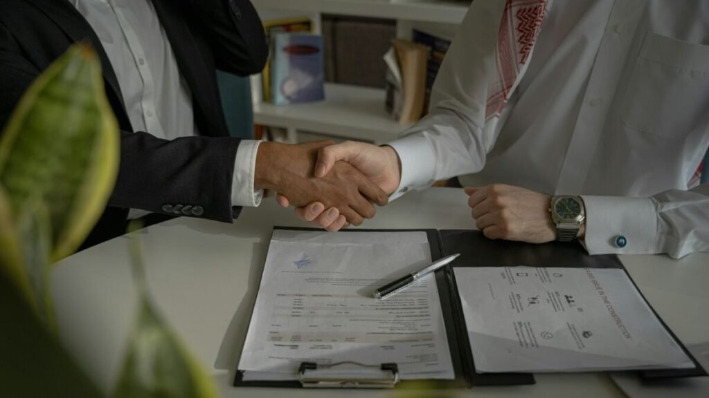 Dos personas se dan la mano sobre documentos de trabajo.